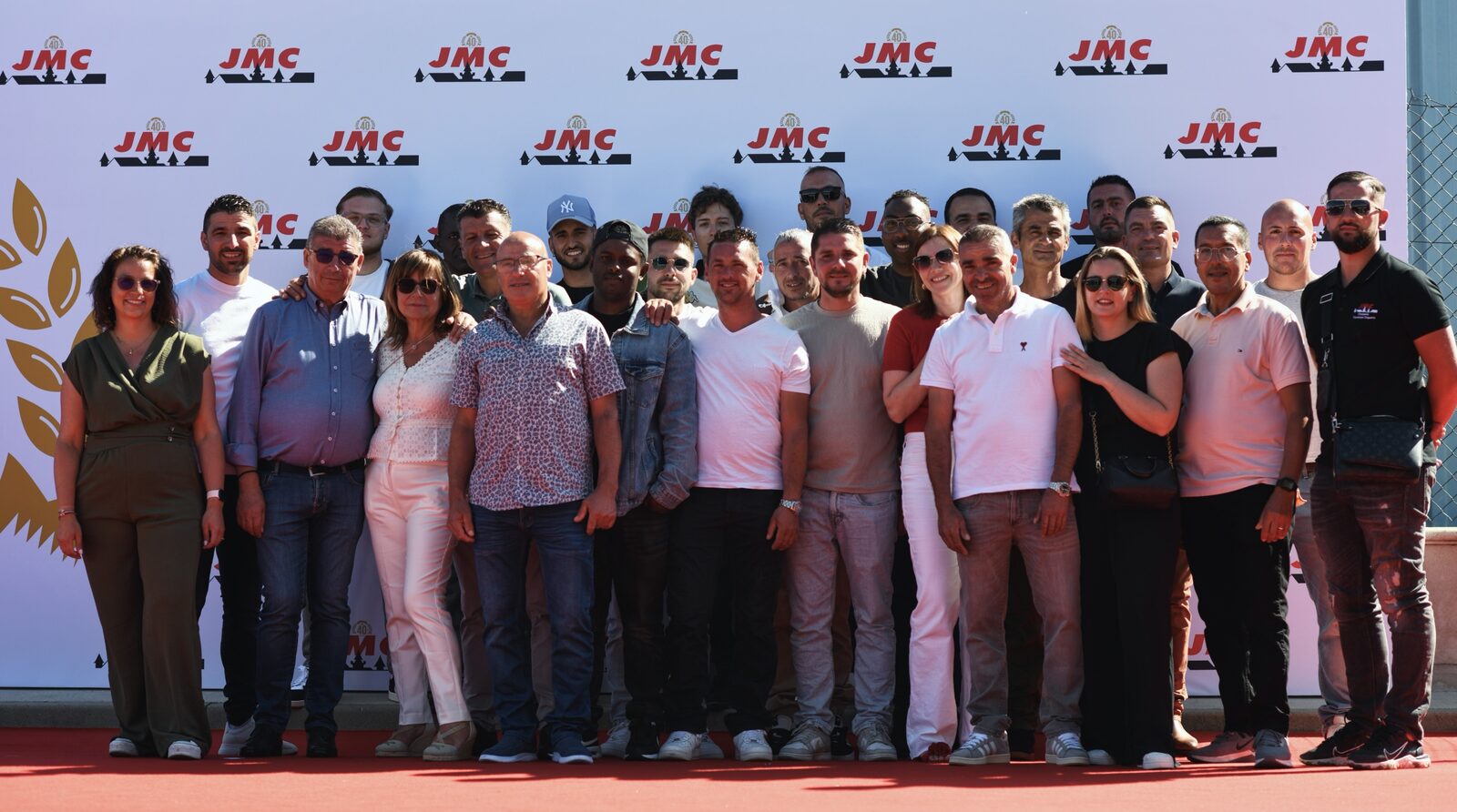 L'équipe de JMC Couverture réunie devant un mur aux couleurs de l'entreprise pour ses 40 ans : couvreurs, charpentiers, zingueurs, encadrement et direction